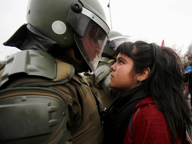 Jovem encara policial em Santiago neste domingo (11) (Foto: Carlos Vera/Reuters)